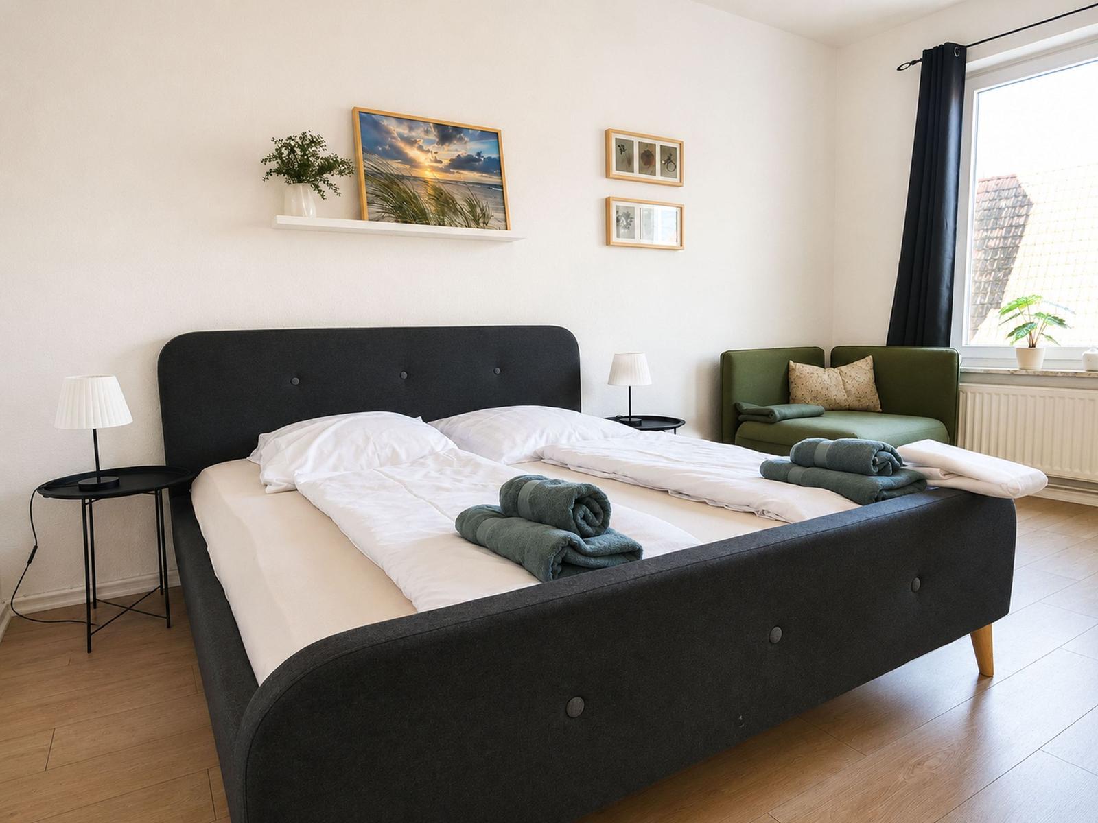 Schlafzimmer mit Doppelbett, grünem Sofa und Fenster mit Blick.