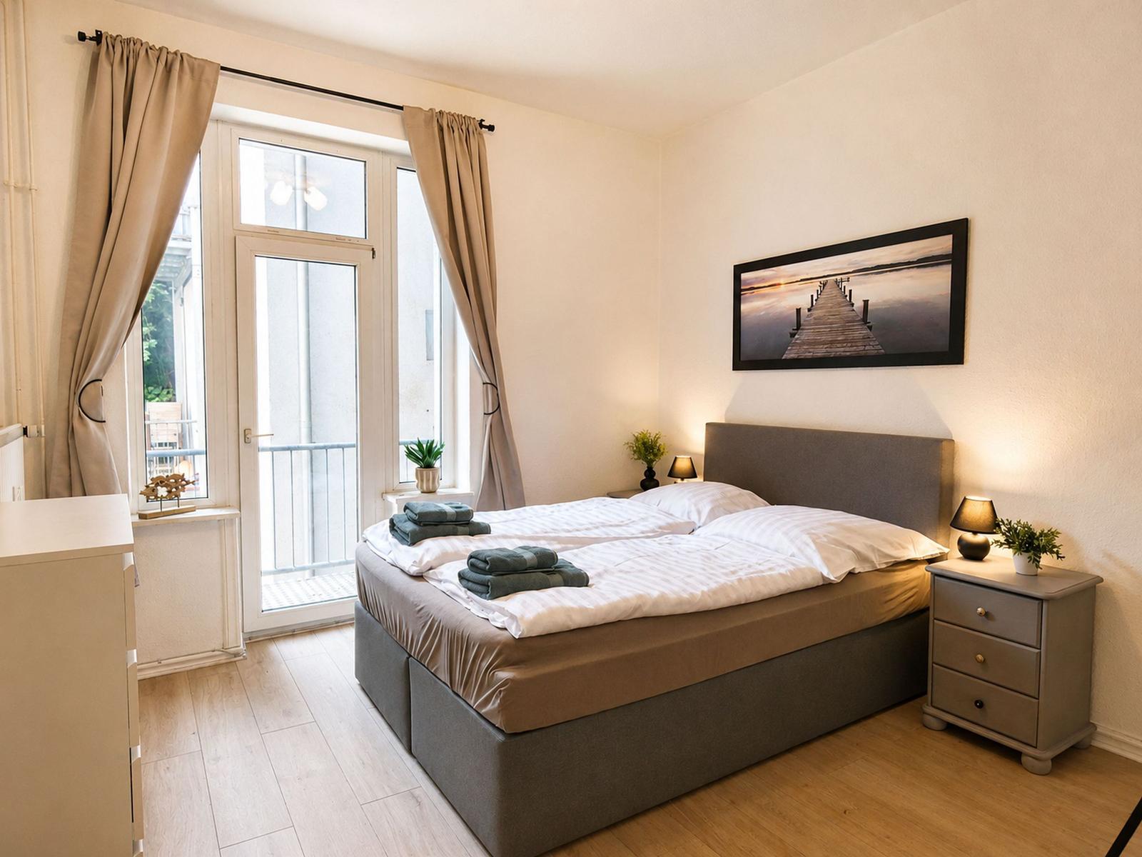 Schlafzimmer mit Doppelbett, Fenster zur Terrasse und Nachttischen mit Lampen.