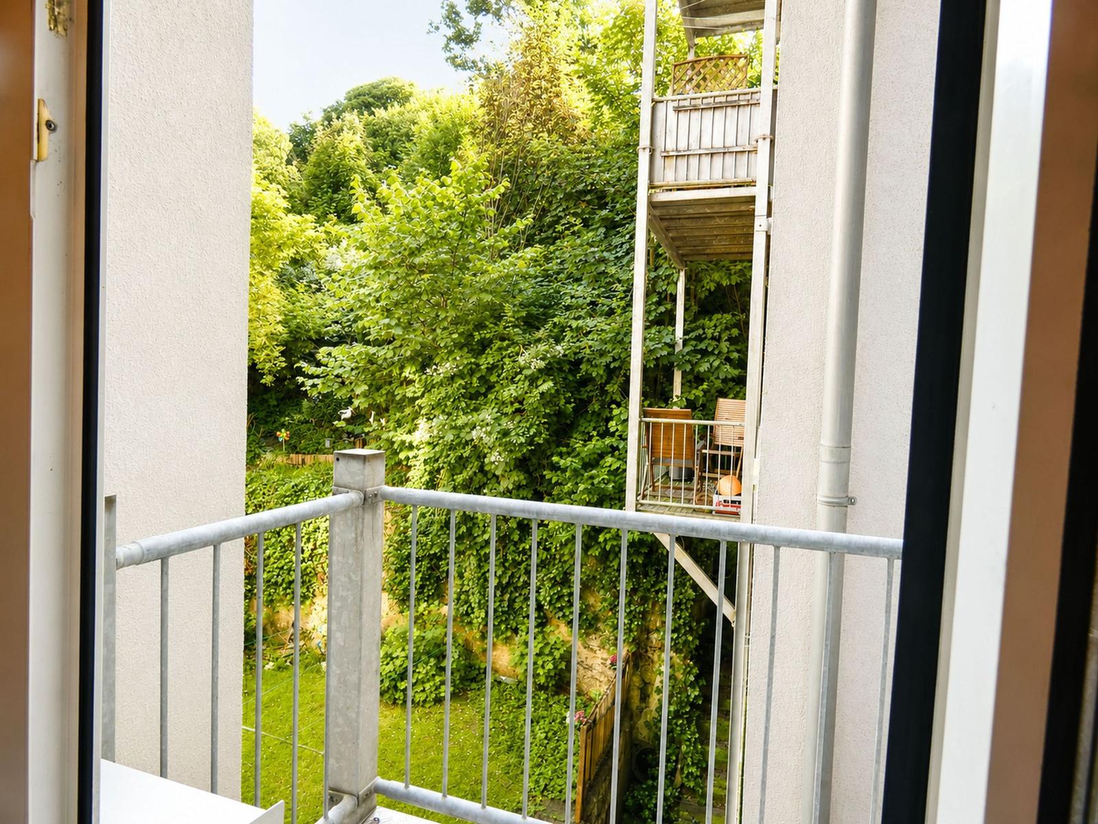 Balkon mit Metallgeländer blickt auf grüne Bäume und einen angrenzenden Balkon.