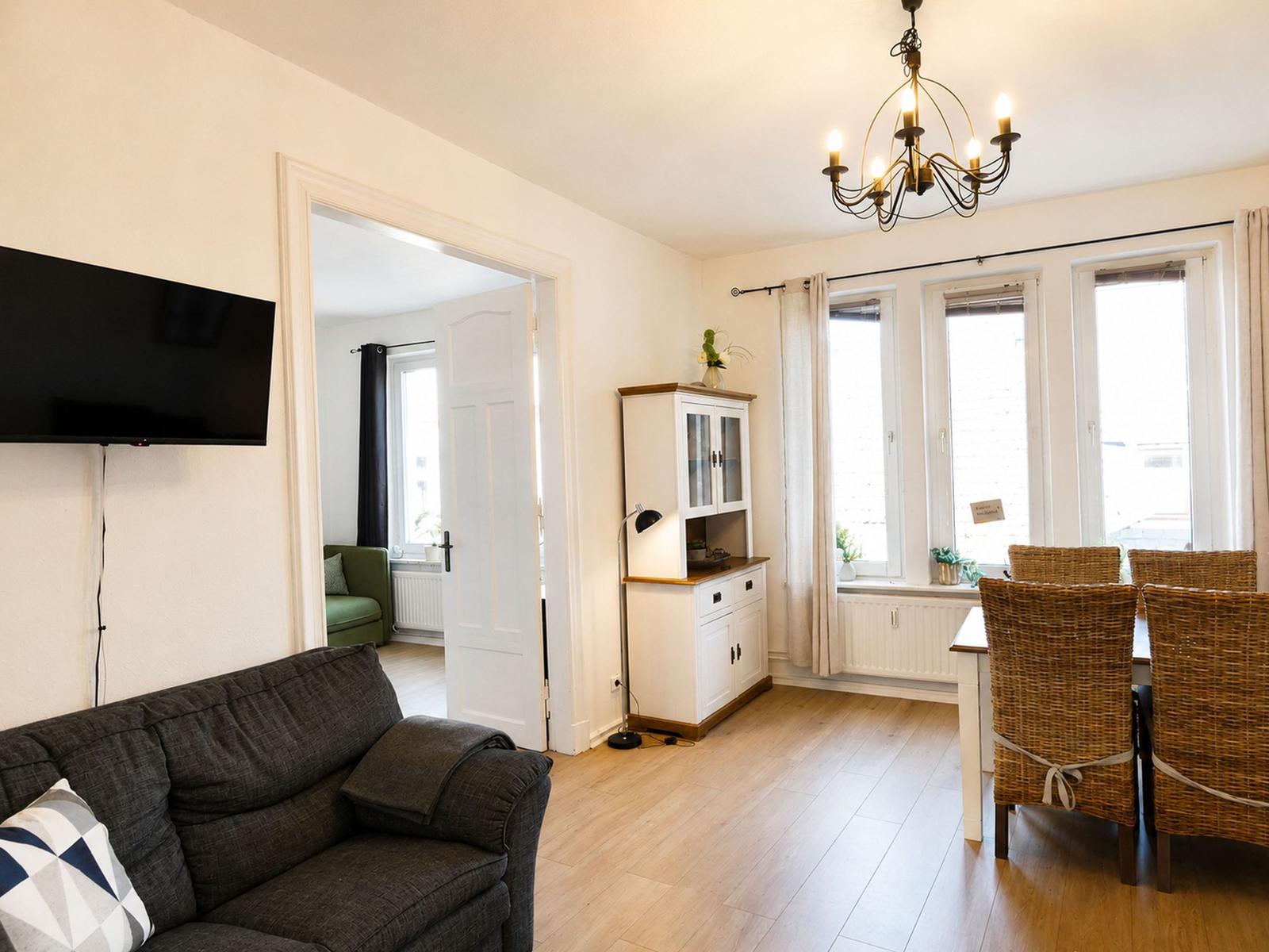 Wohn- und Essbereich mit Sofa, TV, Esstisch und Fenstern.