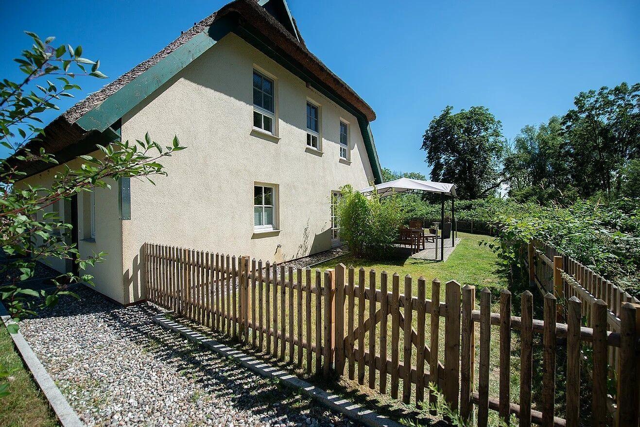 Haus mit Strohdach, Holzzaun und Garten mit Pavillon.