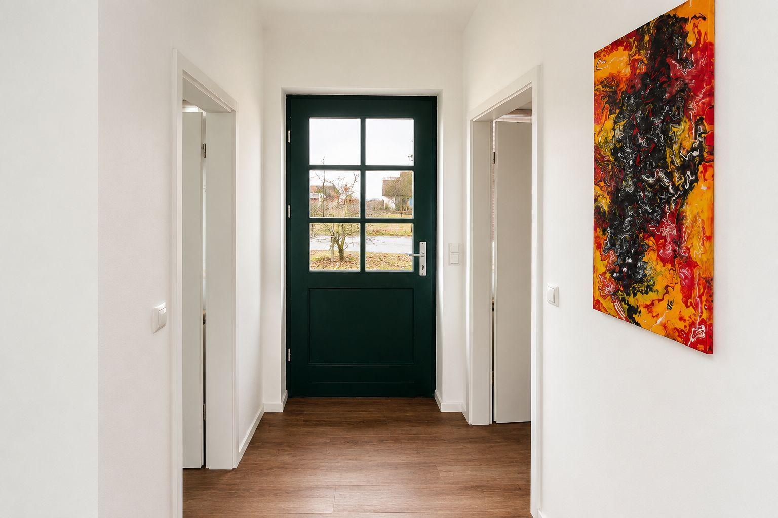 Hausflur mit dunkelgrüner Eingangstür und abstraktem Gemälde an der Wand.