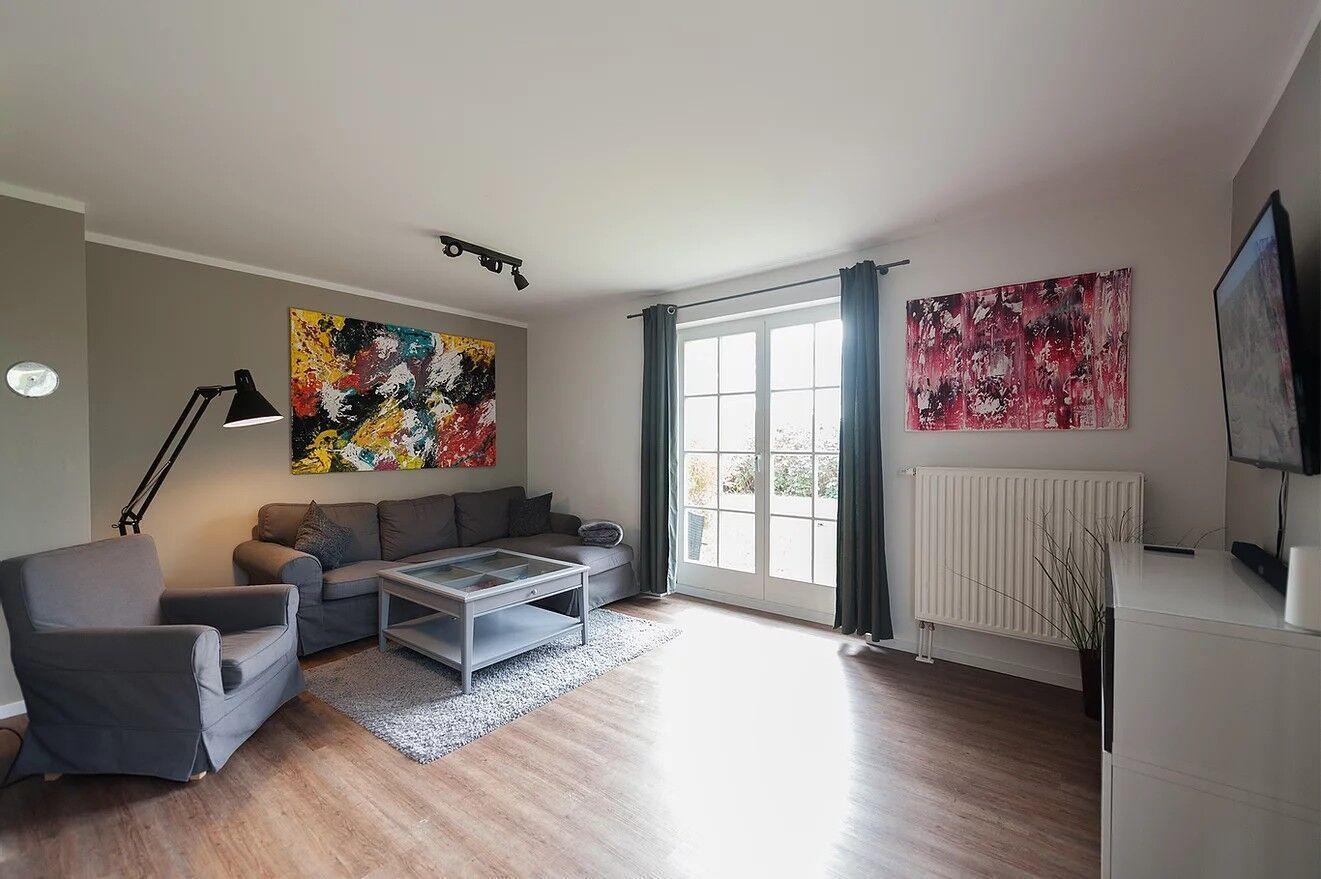 Wohnzimmer mit Sofa, Sessel, Couchtisch und großen Fenstern.