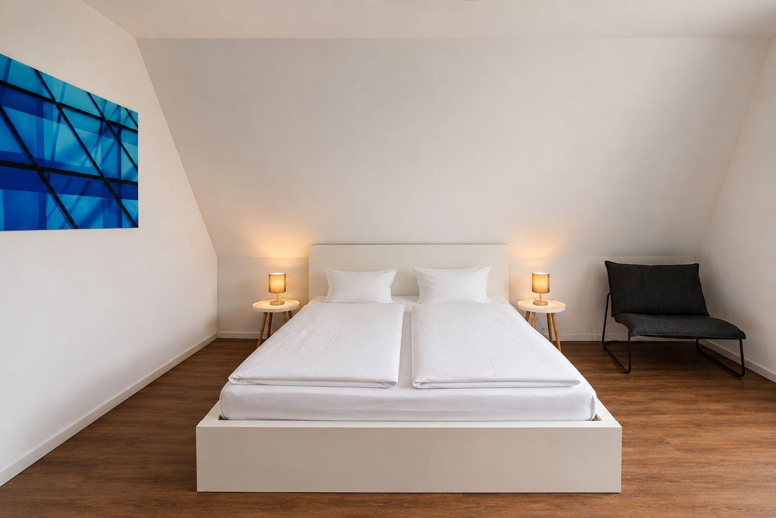 Schlafzimmer mit Doppelbett, zwei Nachttischen und einem Stuhl an der Wand.