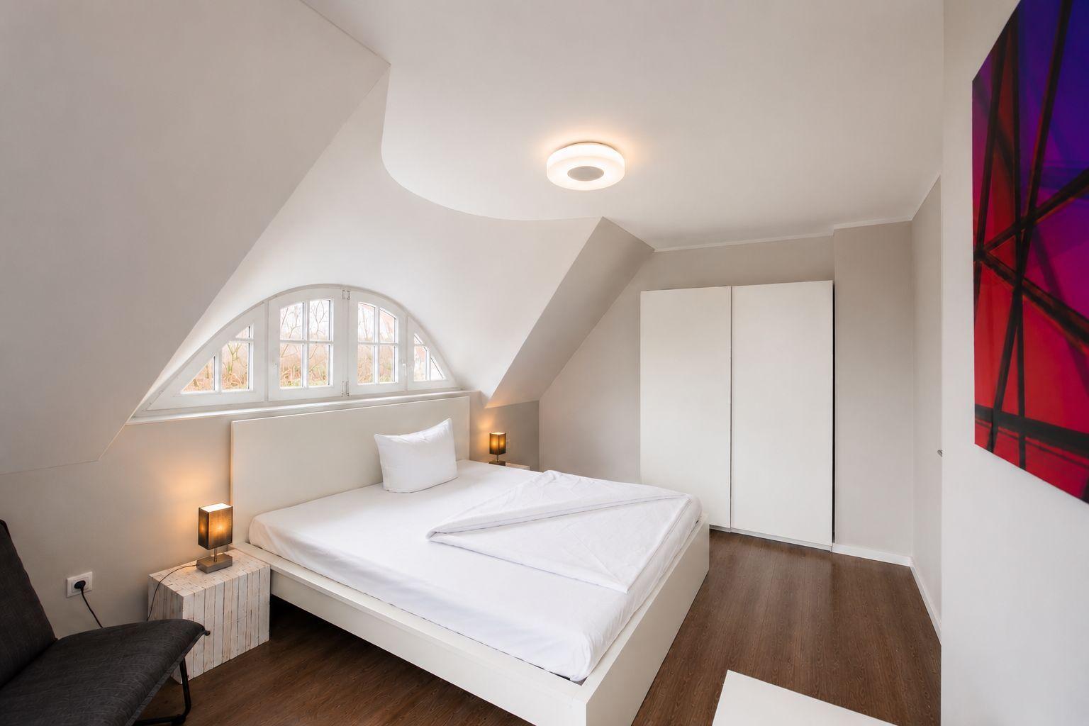 Schlafzimmer mit Dachschräge, Bett, Schrank und Fenster