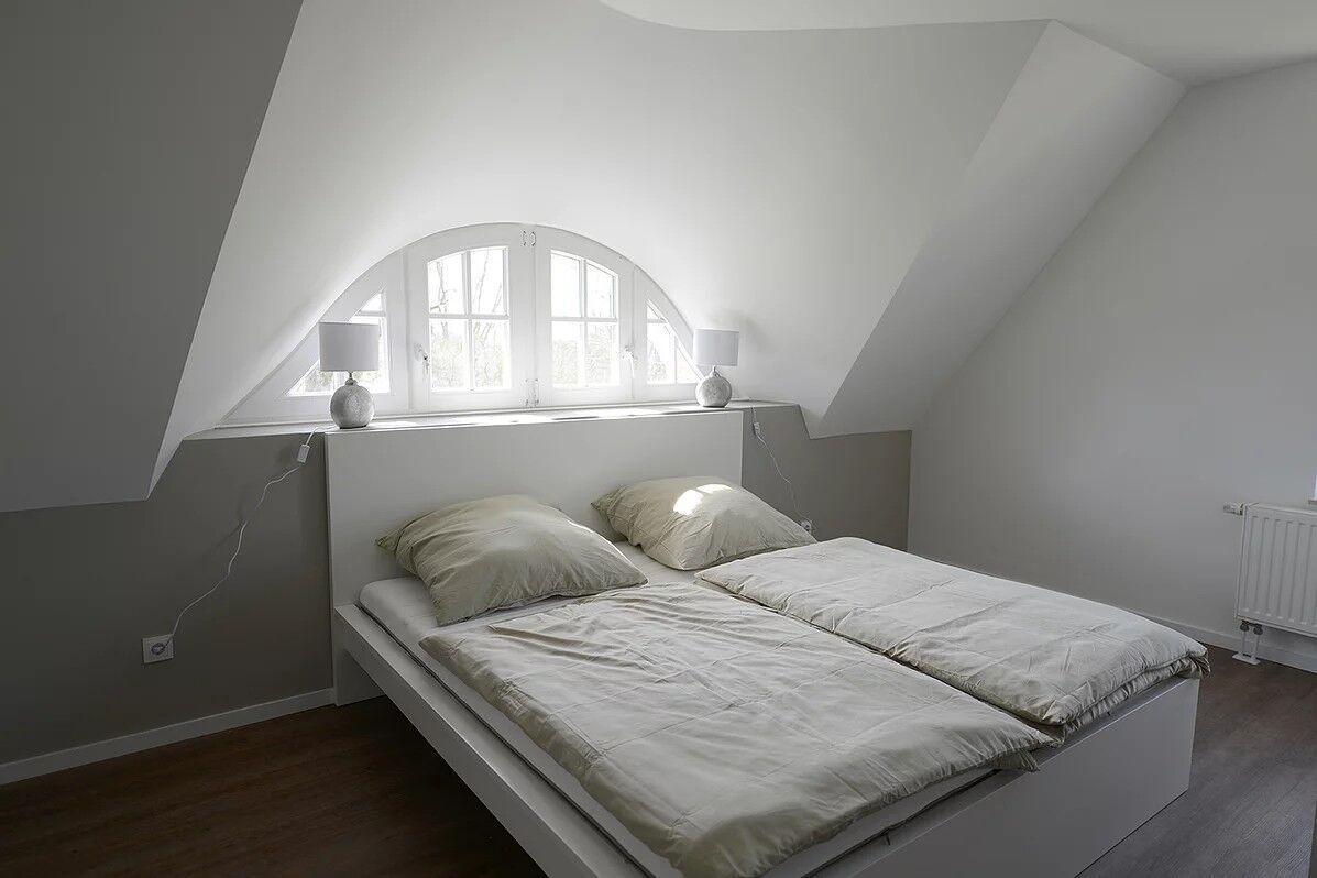 Schlafzimmer mit Doppelbett, Bogenfenster und weißen Lampen an der Wand.