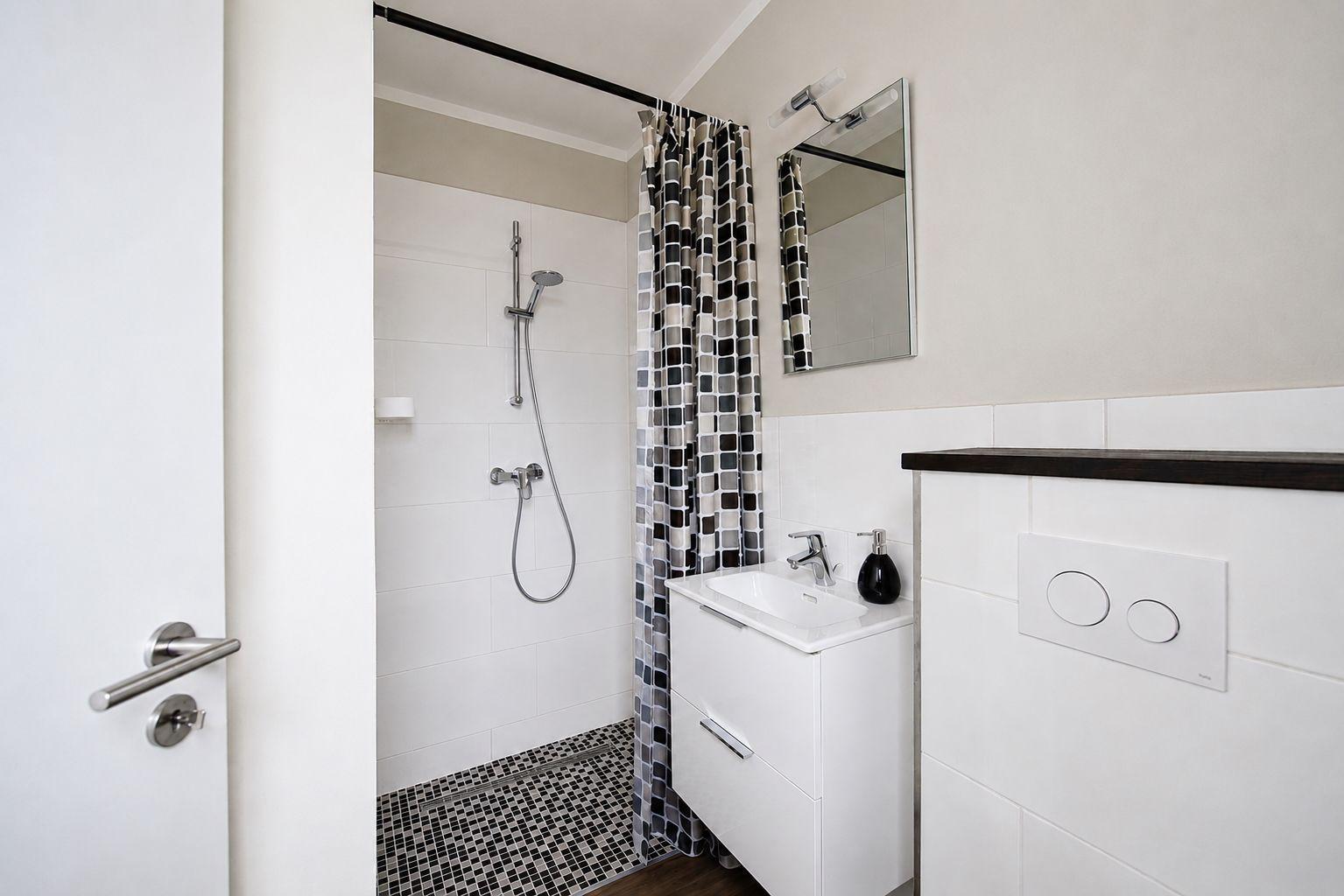 Badezimmer mit Dusche, Waschbecken und Spiegel.