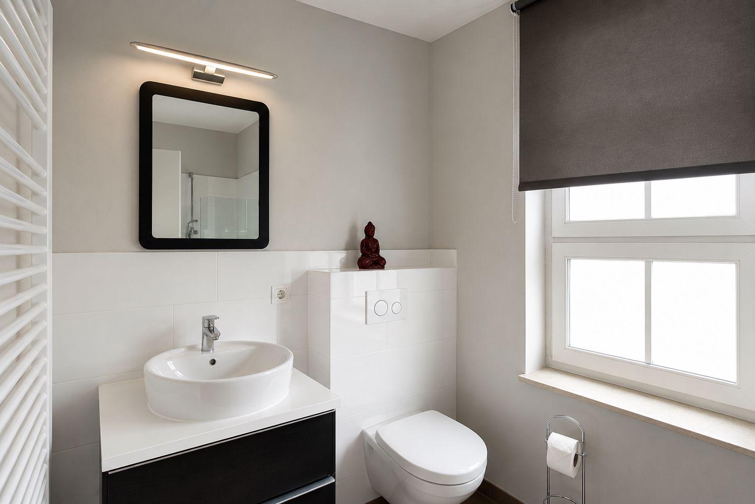 Badezimmer mit Waschbecken, Toilette und Fenster mit Rollladen.