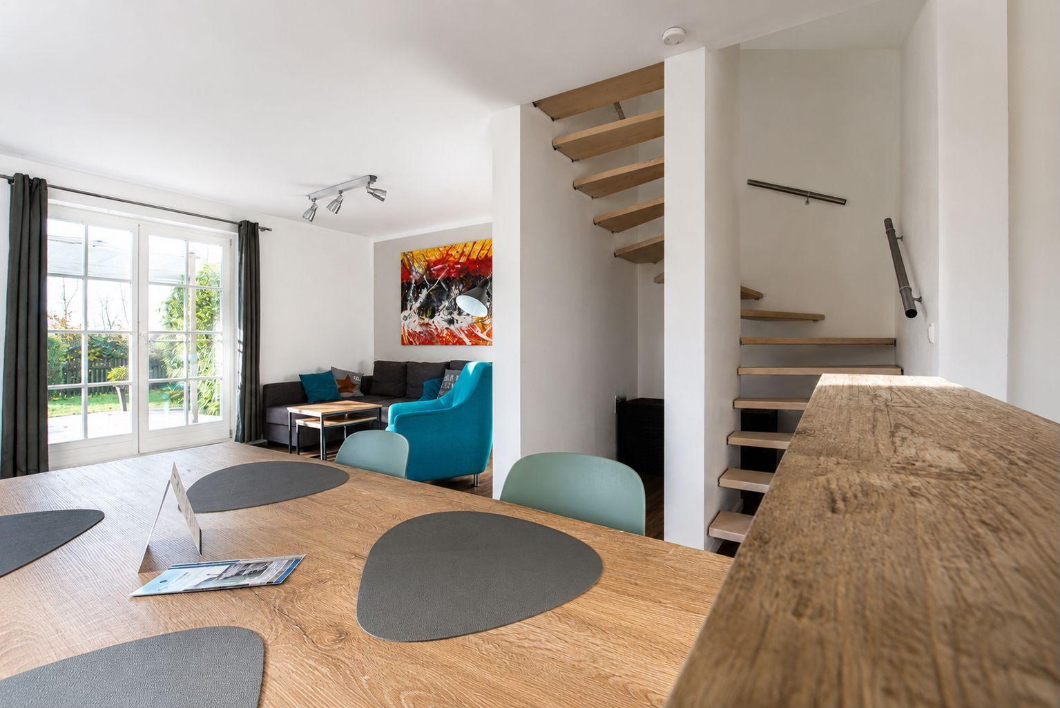 Essbereich mit Holztisch, Stühlen und Blick auf Wohnzimmer mit Sofa und Treppe.