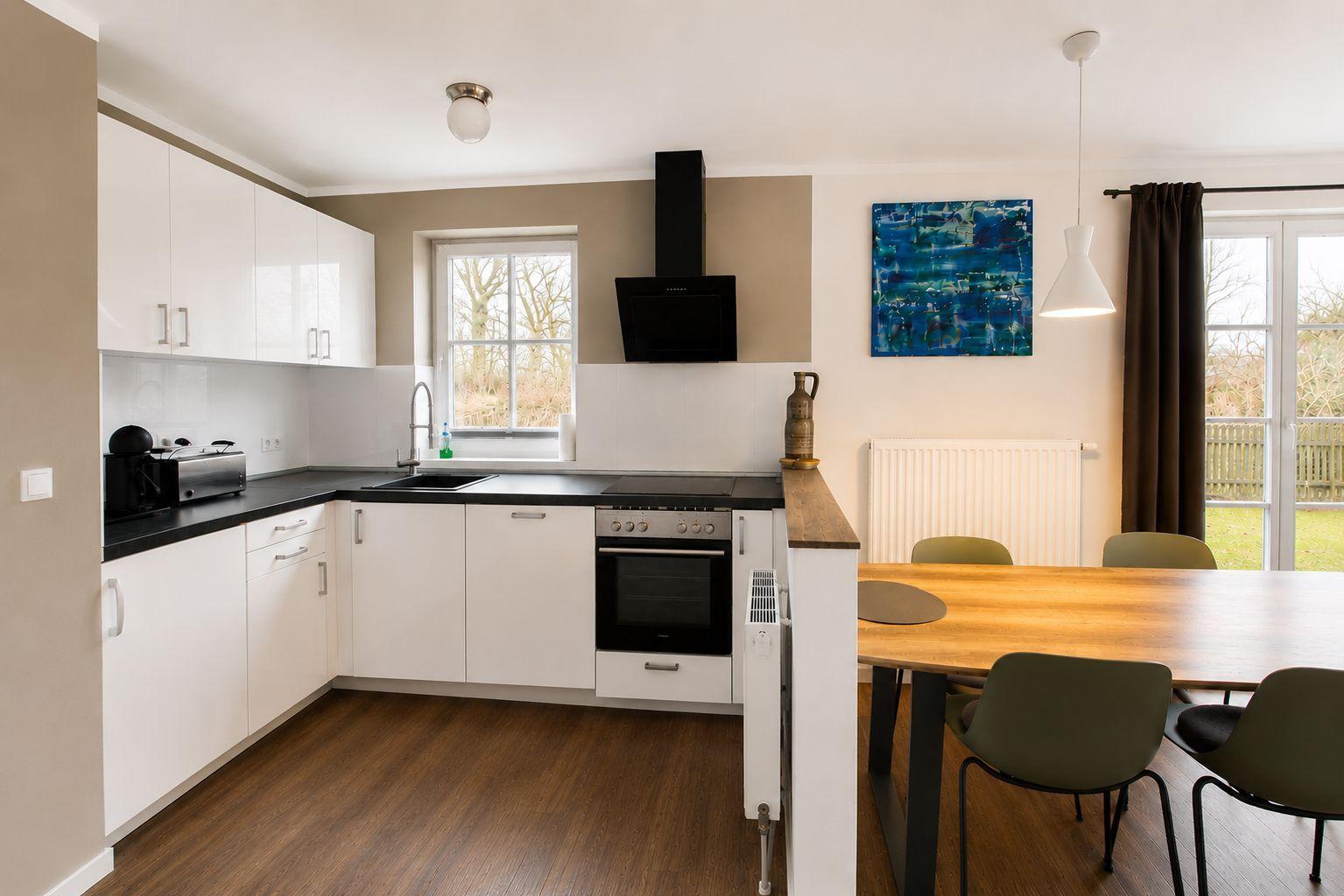 Küche mit Essbereich, schwarze Arbeitsplatte, weiße Schränke und Holzfußboden.