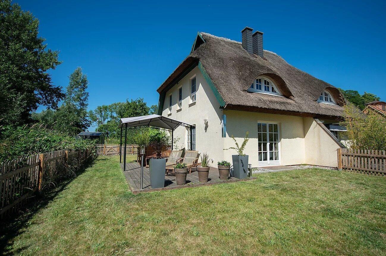Haus mit Strohdach, Garten und Terrasse mit Sitzgelegenheiten.