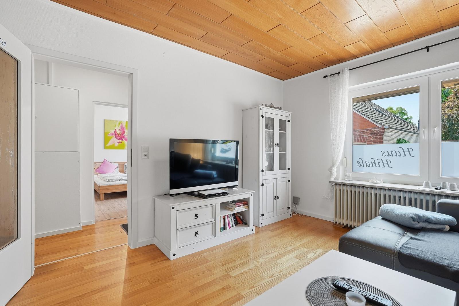 Wohnzimmer mit Holzdecke, Fernseher und Blick in Schlafzimmer.