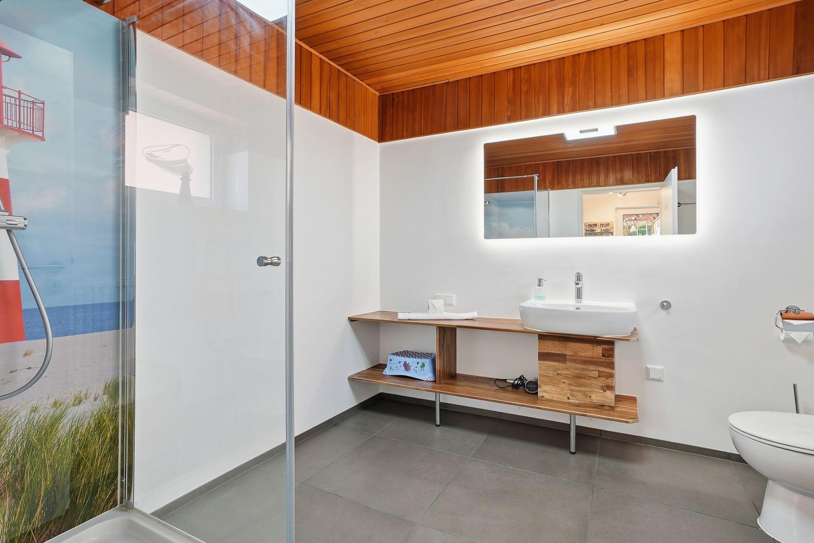 Badezimmer mit Dusche, Waschbecken und Toilette. Holzdecke und -möbel.