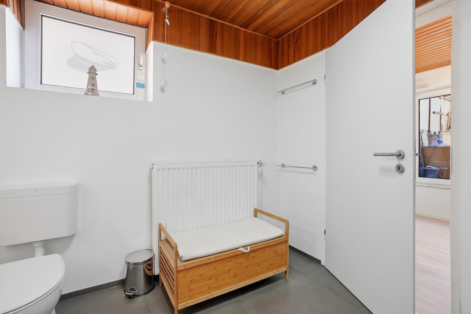 Badezimmer mit Toilette, Holzbank und Fenster mit Seesternmotiv.