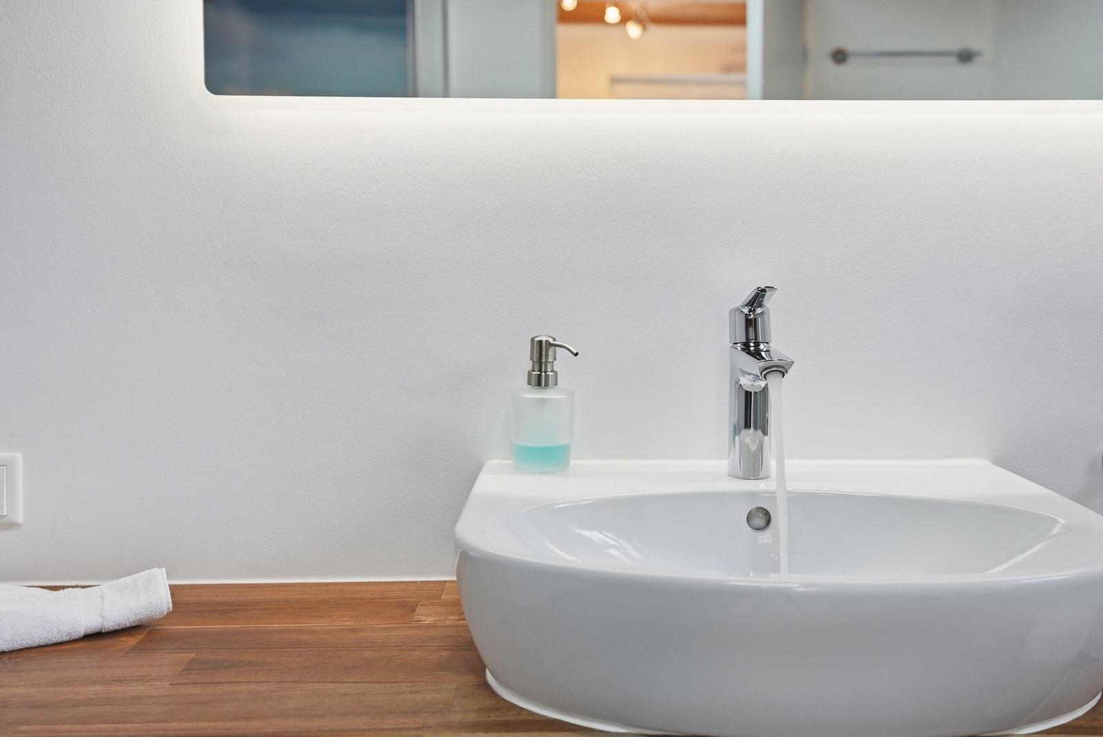 Waschbecken mit laufendem Wasser, Seifenspender und Spiegel im Badezimmer.