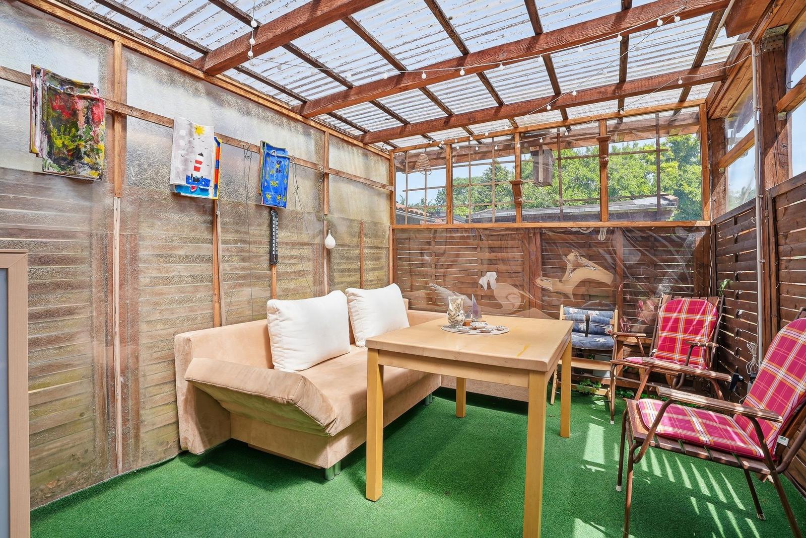 Terrassenbereich mit Sofa, Tisch und Stühlen unter Glasdach.