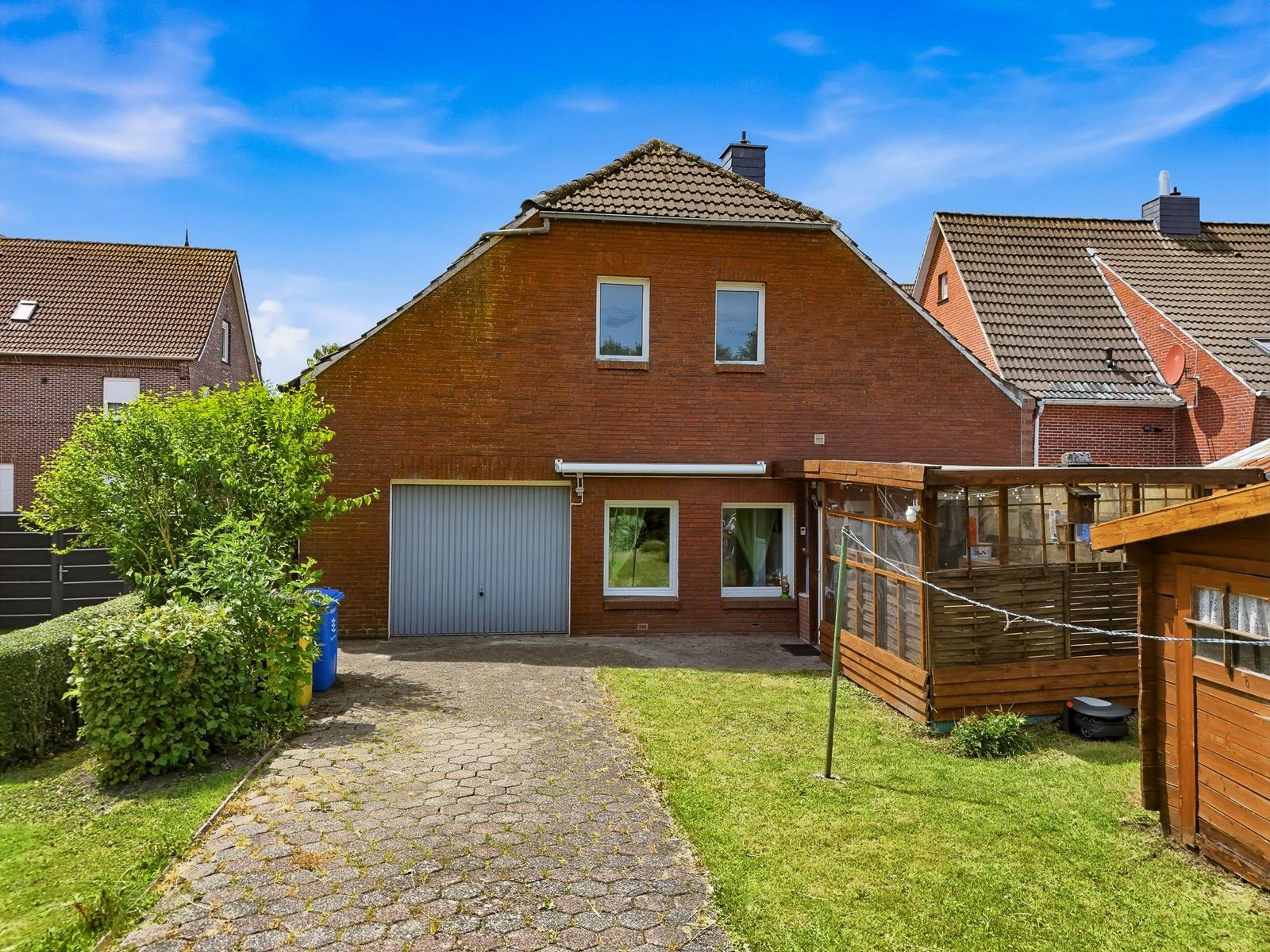 Rotes Backsteingebäude mit Garage und Gartenhaus. Grünflächen und gepflasterter Weg.