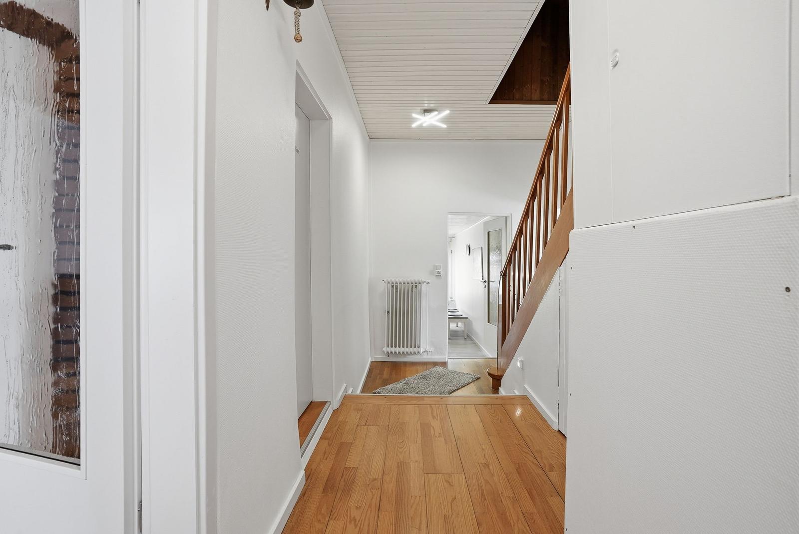 Flur mit Holzboden, Treppe und Heizkörper. Weiße Wände und Decke.