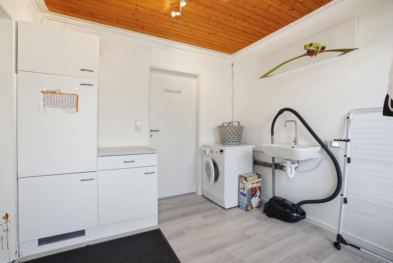 Wohnraum mit Waschmaschine, Spüle und Trockner. Holzdecke und weiße Möbel.