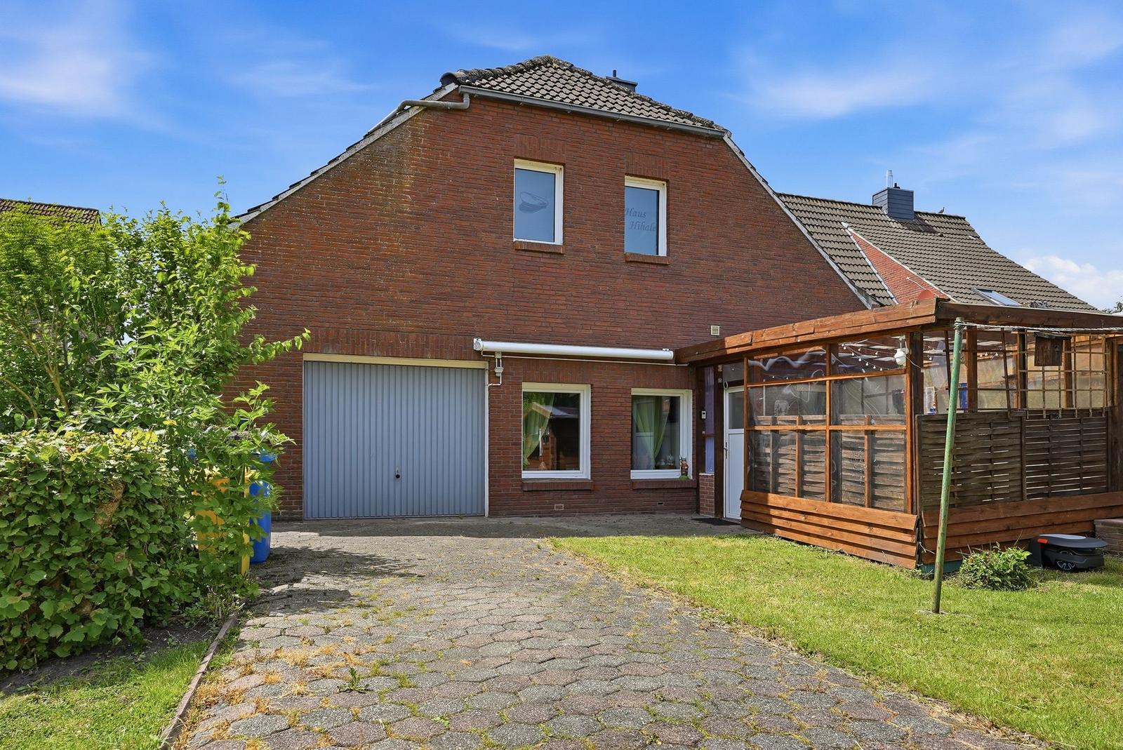 Rotes Backsteingebäude mit Garage und Holzveranda. Grasfläche und Kiesweg.