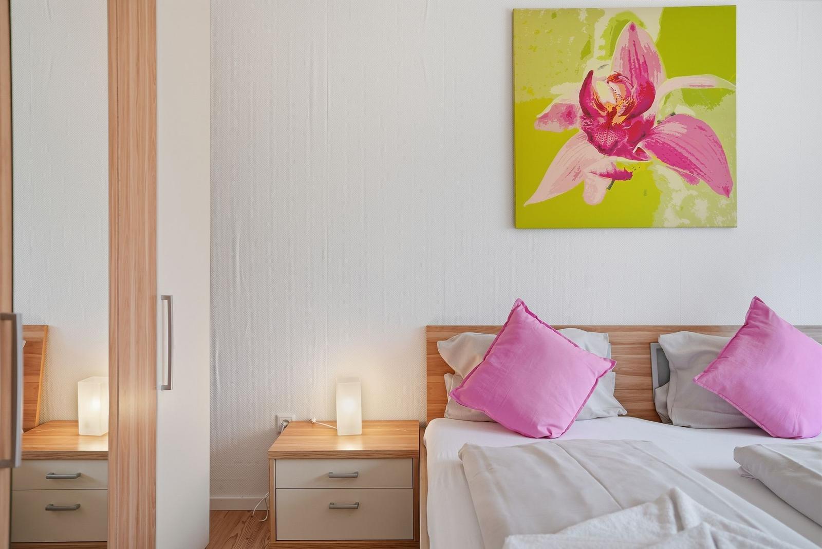 Schlafzimmer mit Bett, Nachttisch und Wandbild einer Orchidee.