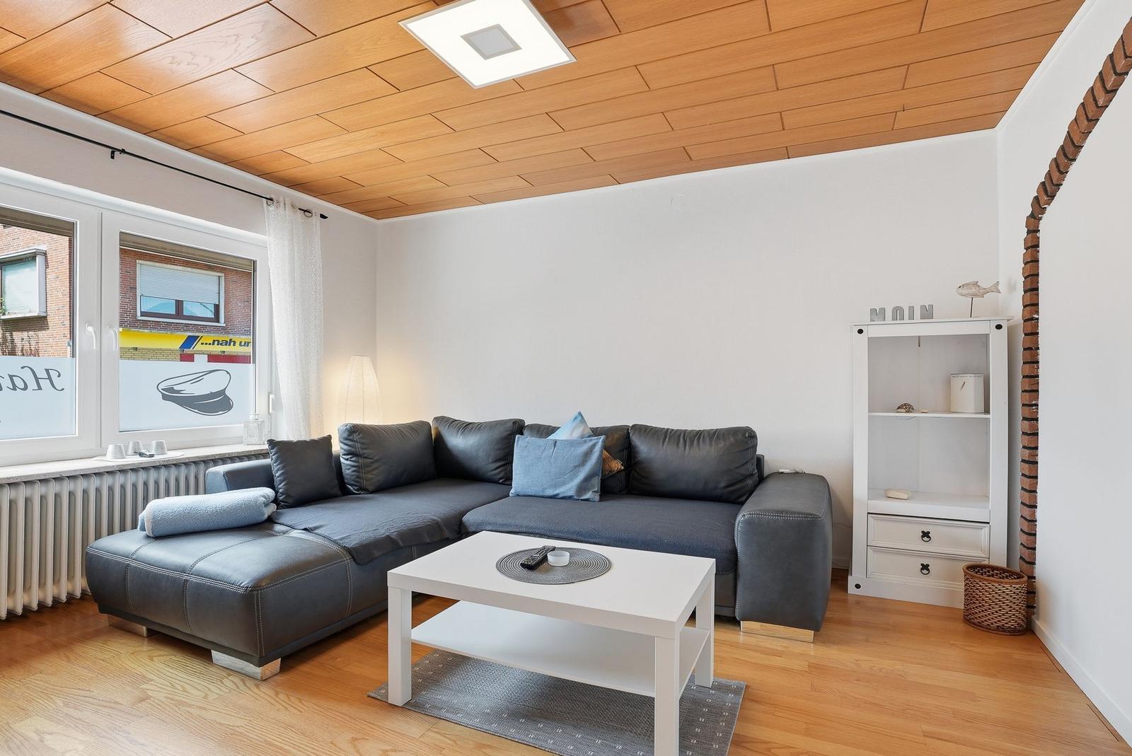 Wohnzimmer mit grauem Sofa, weißem Couchtisch und Holzdecke.