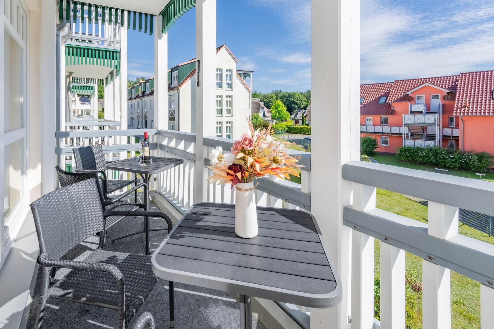 Terrasse mit Tisch, Stühlen und Blumenvase. Blick auf Wohnhäuser und Grünflächen.