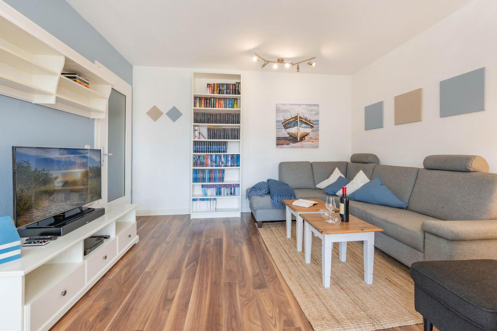 Wohnzimmer mit Sofa, Bücherregal, Fernseher und Holzboden.