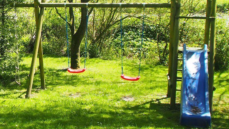 Hinterhof mit Spielplatz, Schaukel und Rutsche auf grünem Rasen.