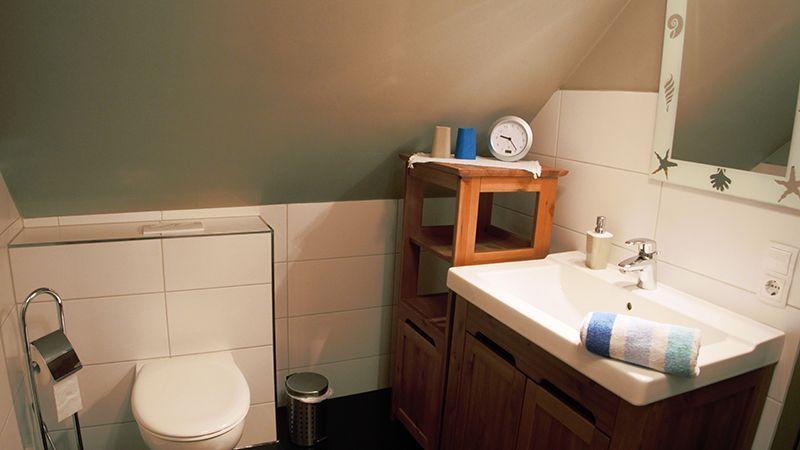 Badezimmer mit Toilette, Waschbecken und Holzregal unter Dachschrägen