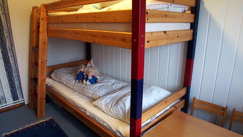 Ein Doppelstockbett mit Holzgestell und roten Säulen. Auf dem unteren Bett liegen zwei Plüschtiere.