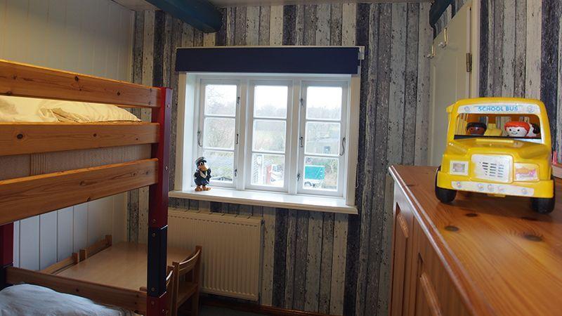 Zimmer mit Doppelstockbett, Fenster und Holzmöbel. Auf Schreibtisch steht ein gelber Bus.