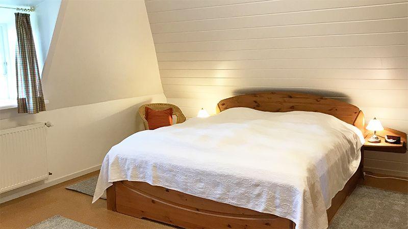 Schlafzimmer mit Holzbett, Nachttischen und Fenster. Wandverkleidung und Heizung sichtbar.