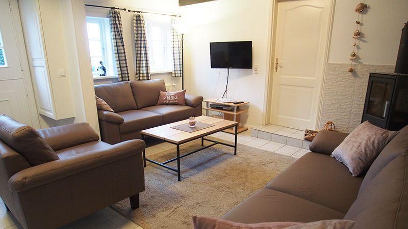 Wohnzimmer mit Sofa, Sessel und Fernseher an der Wand.