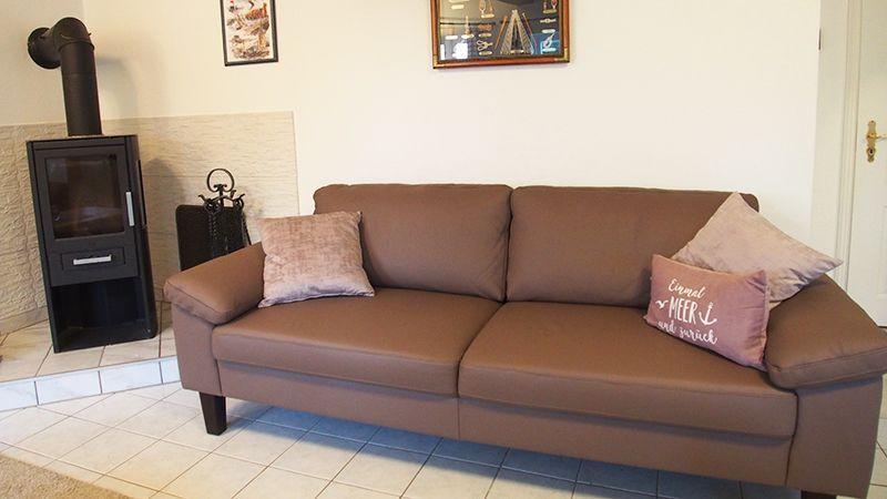 Ein braunes Sofa mit Kissen steht vor einer Wand mit Kaminofen und Bildern.