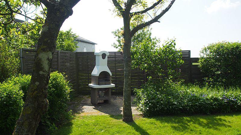 Garten mit Grill, Bäumen und Hecke. Hintergrund zeigt ein Haus.