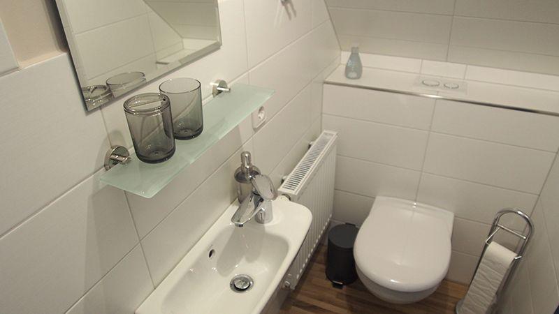 Badezimmer mit Waschbecken, Spiegel, Toilette und Handtuchhalter.
