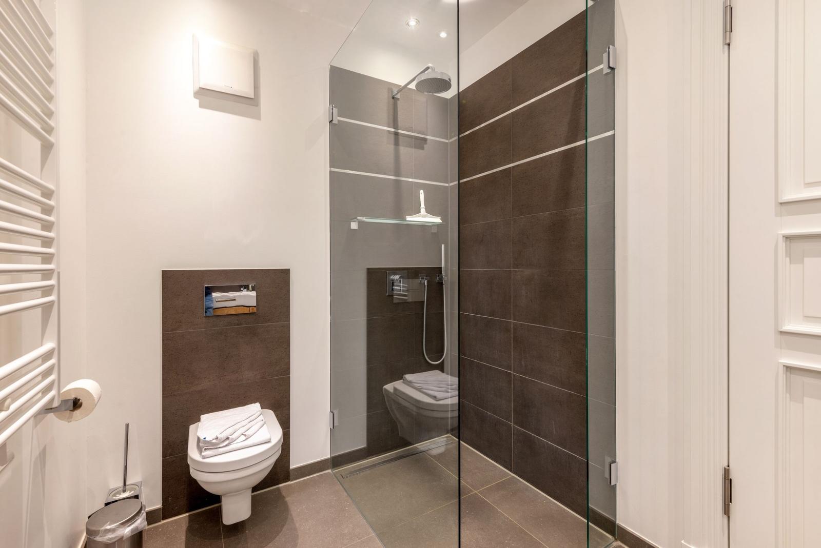 Badezimmer mit Dusche, Toilette und Heizung. Fliesen und Spiegel sichtbar.