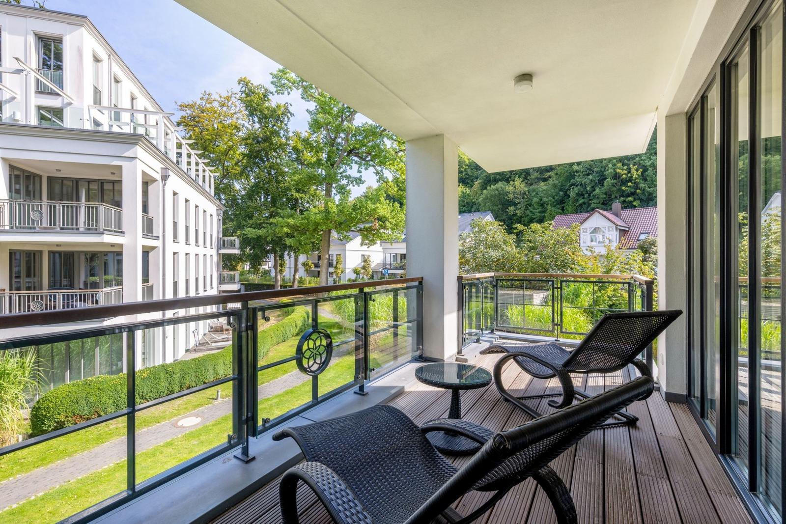 Terrasse mit Liegestühlen und Tisch. Blick auf grüne Landschaft und Gebäude.