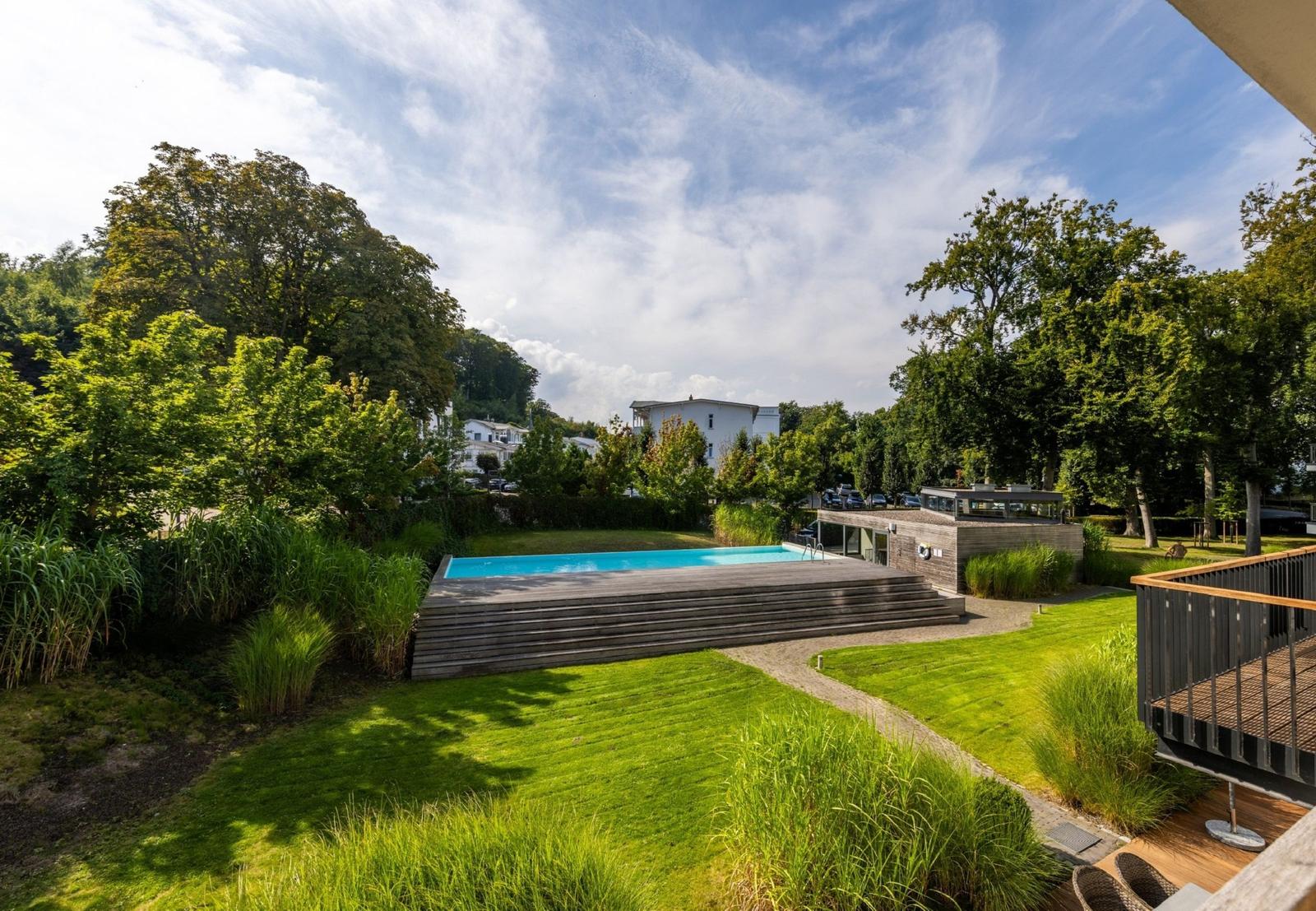 Pool mit Terrasse und Grünflächen im Garten. Blick auf umliegende Bäume und Gebäude.