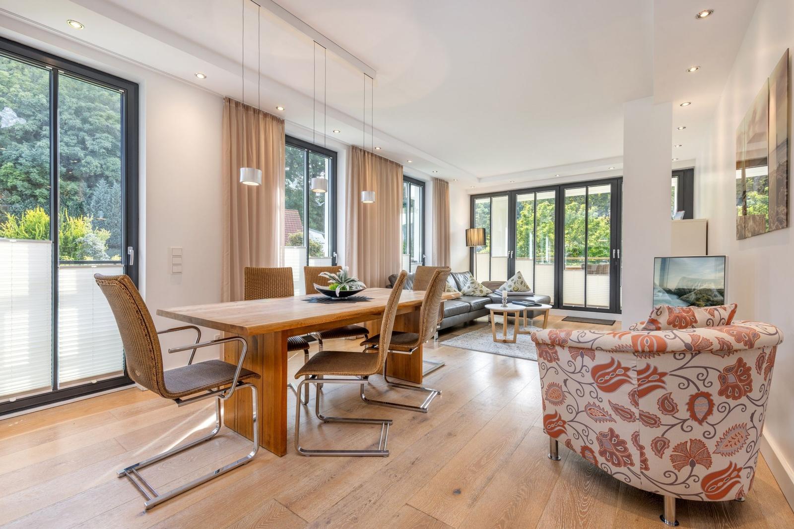 Essbereich mit Tisch und Stühlen, Wohnbereich mit Sofa und Sessel, große Fenster mit Blick auf Garten.