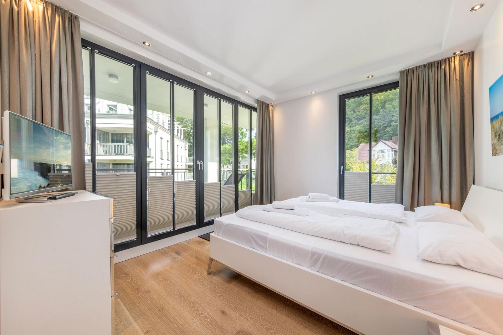 Schlafzimmer mit großem Bett, TV und Fenstern zum Balkon.