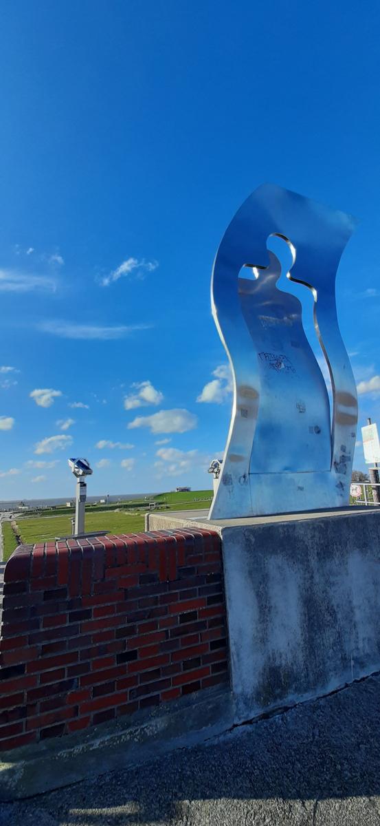 Metallskulptur auf Betonsockel mit Blick auf Grünfläche und Himmel