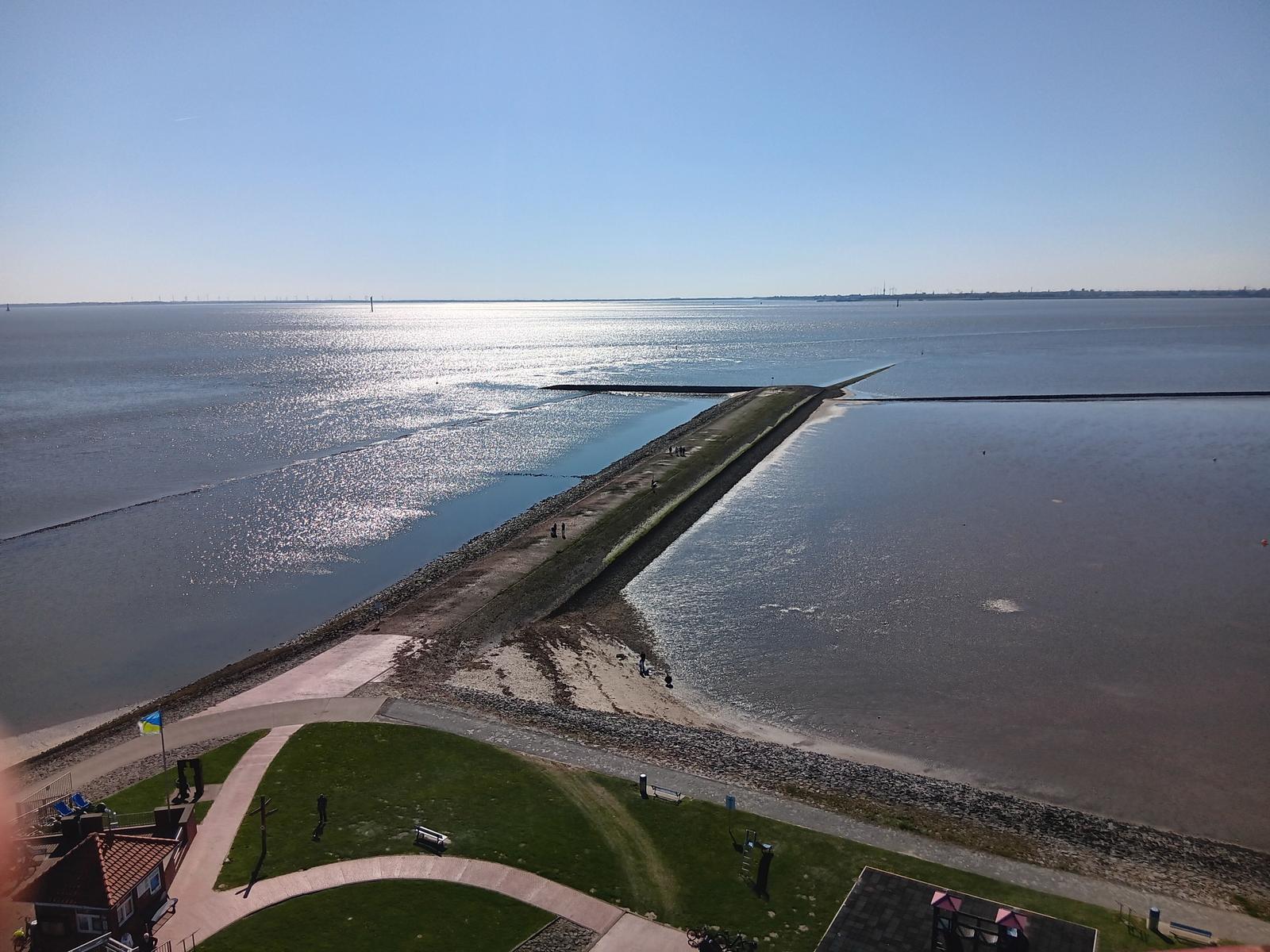 Panoramablick auf einen Deich mit Wasser und Grünflächen im Vordergrund.