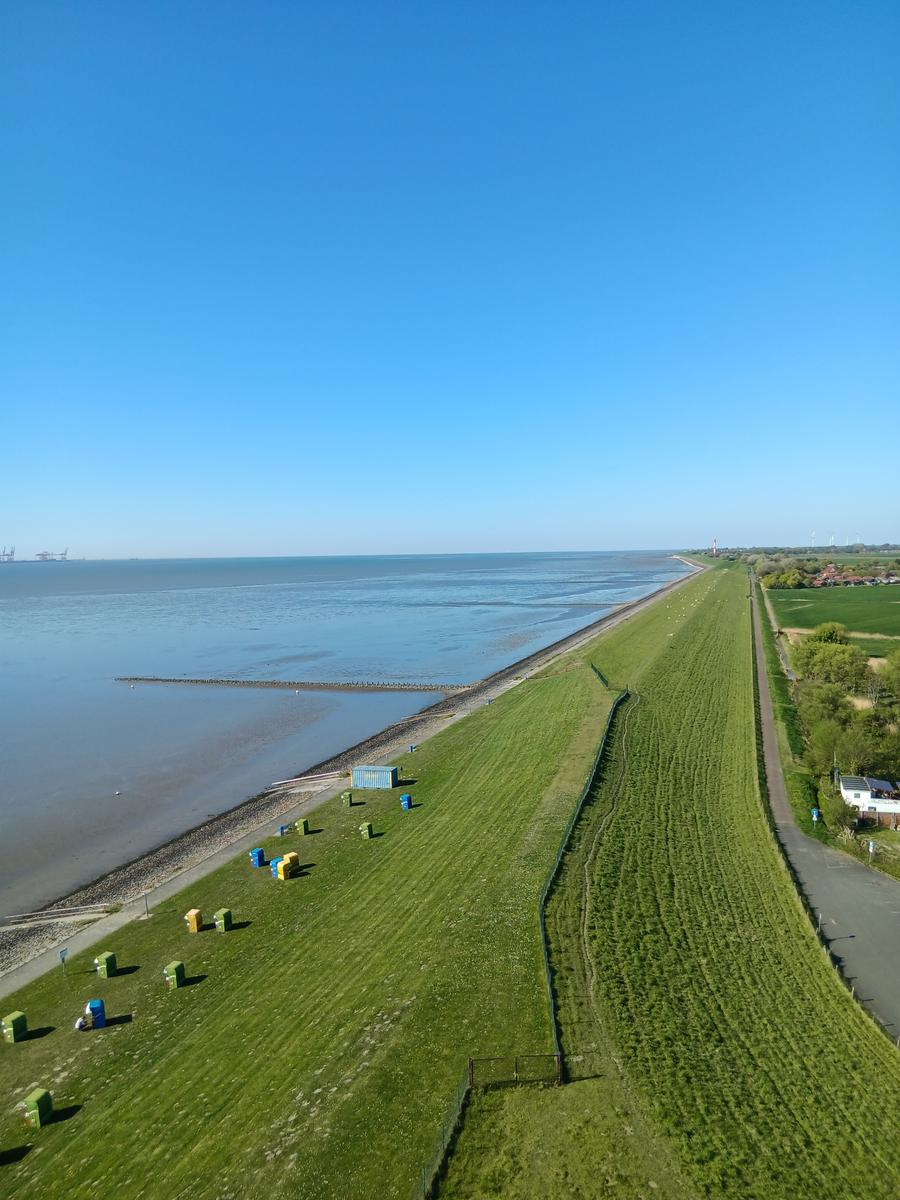 Grüner Deich mit Strandkörben und Blick auf die Nordsee unter blauem Himmel.