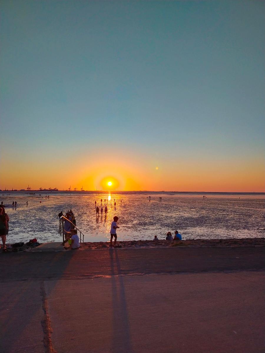 Sonnenuntergang am Strand mit Menschen, die im Wasser stehen und sich entspannen.