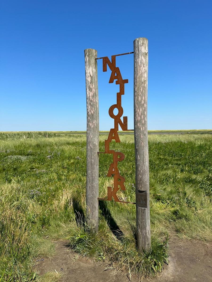 Nationalpark-Schild zwischen zwei Holzpfosten im Grasland unter blauem Himmel