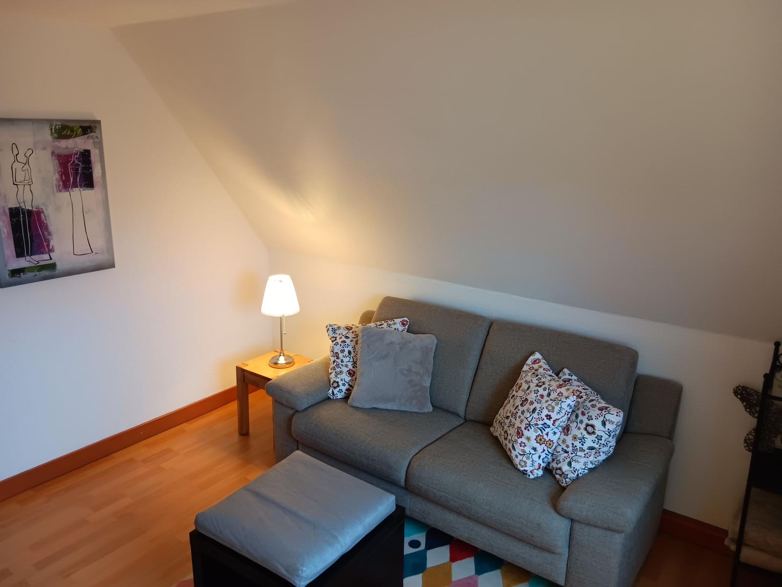 Ein Sofa mit Kissen, Beistelltisch und Lampe unter schrägem Dach.