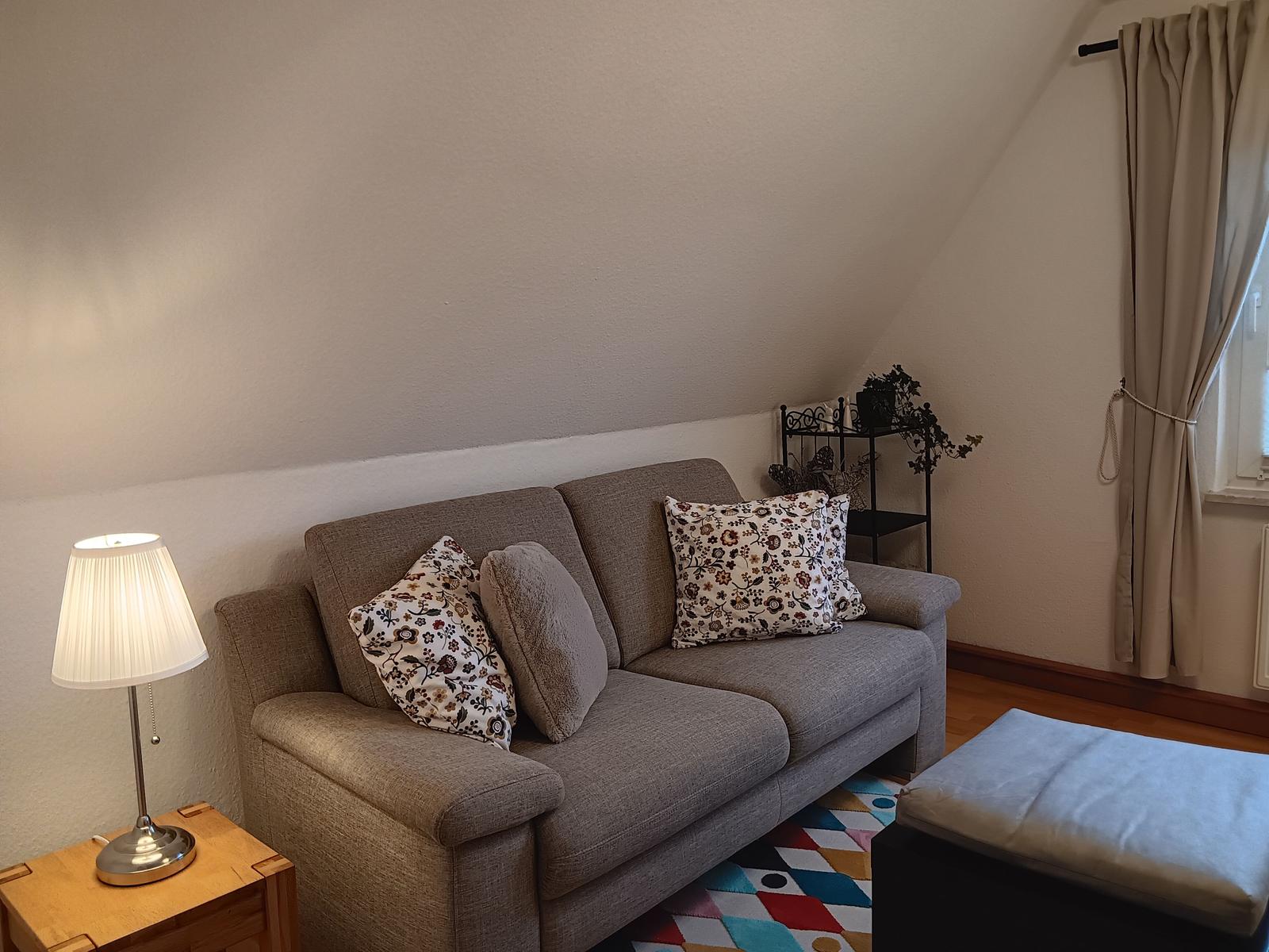Ein Sofa mit Kissen, Beistelltisch und Lampe unter einem Dachschrägen.