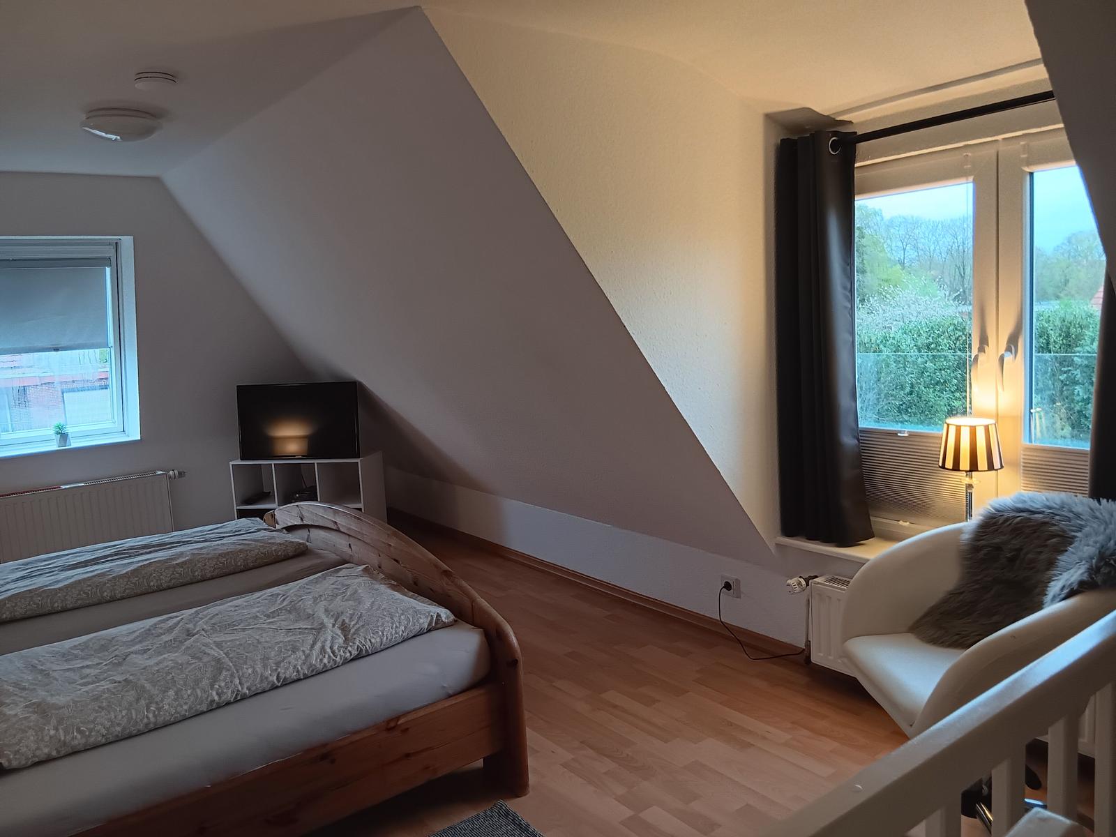 Schlafzimmer mit Dachschrägen, Bett, Sessel und Fenster mit Blick.
